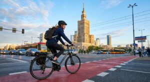 A professional editorial photograph of a modern commuter cycling past the iconic Palace of Culture a