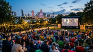 A cinematic wide shot of a bustling open-air cinema setup in a picturesque Warsaw park at dusk, with